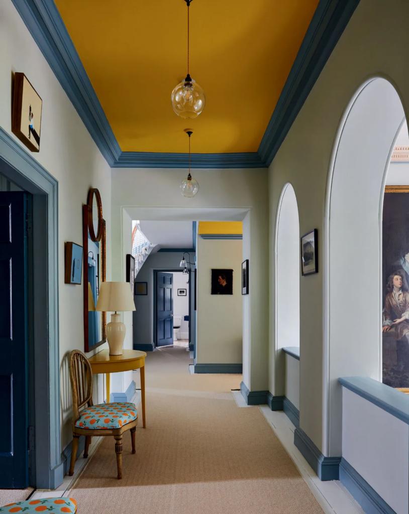 Couloir avec plafond jaune peint, portes bleues et encadrements colorés dans une maison contemporaine.